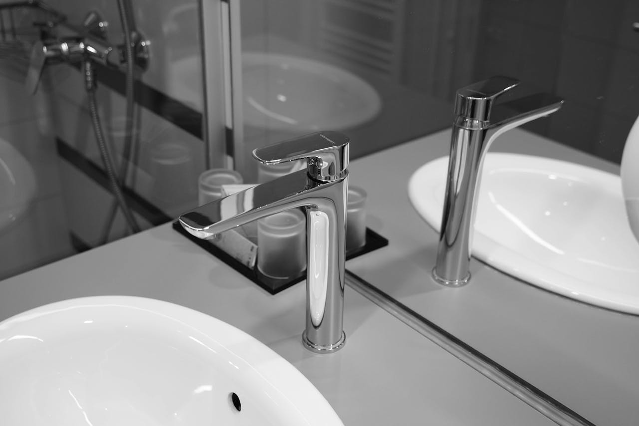 About A sleek stainless steel faucet with reflection in a monochrome bathroom setting, emphasizing modern design.