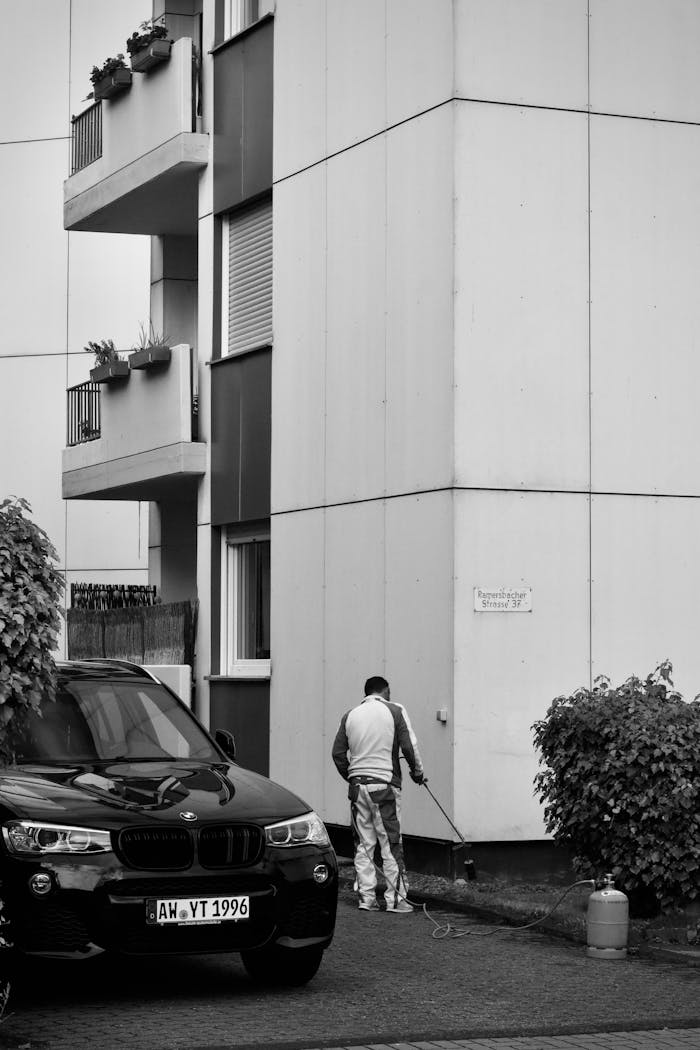 About Black and white photo of a man power washing a building's exterior in a city setting.