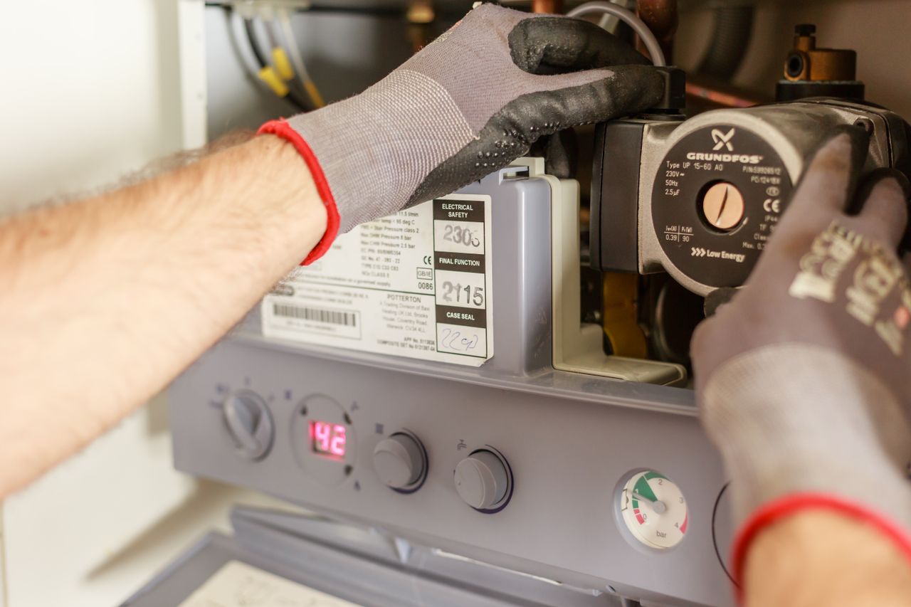 brand-03 Close-up of hands adjusting a boiler system with precise instrumentation, showing maintenance work.