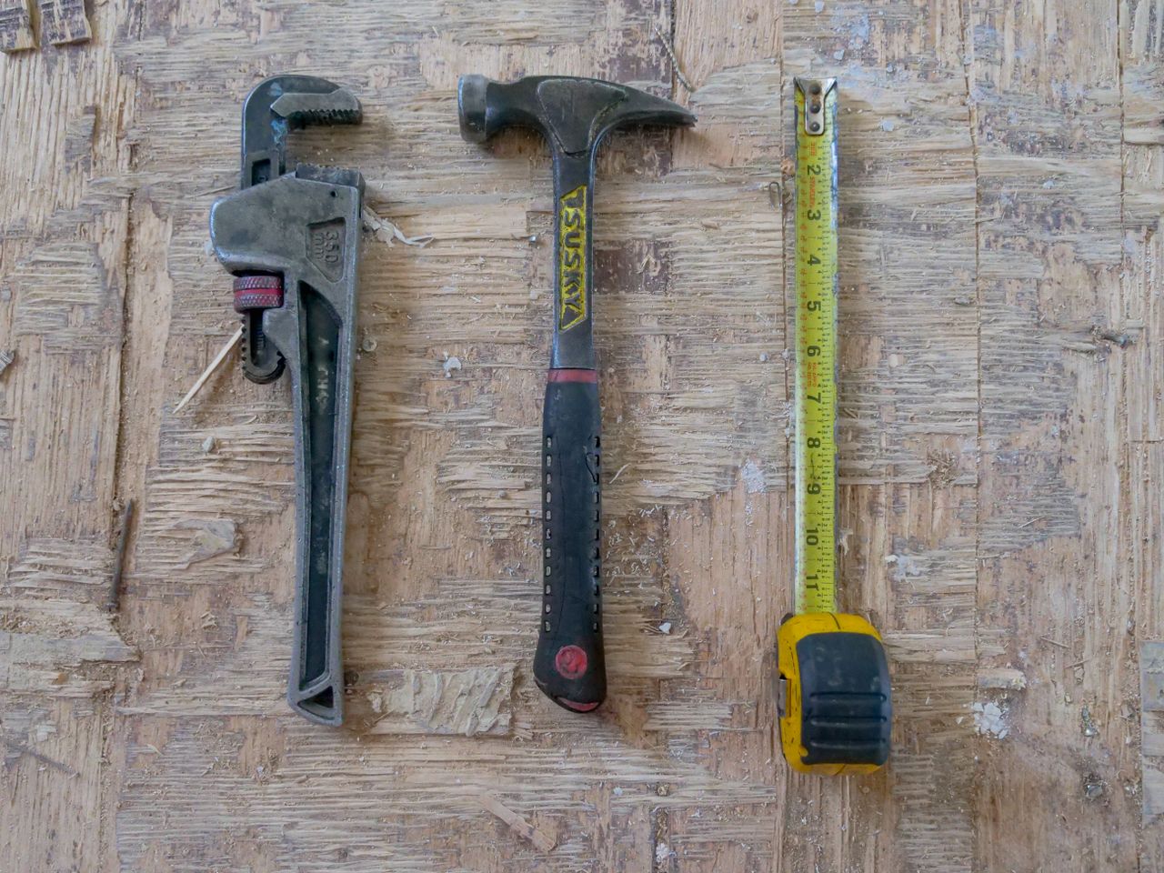 brand-01 Close-up of hammer, wrench, and measuring tape on wooden surface for construction use.