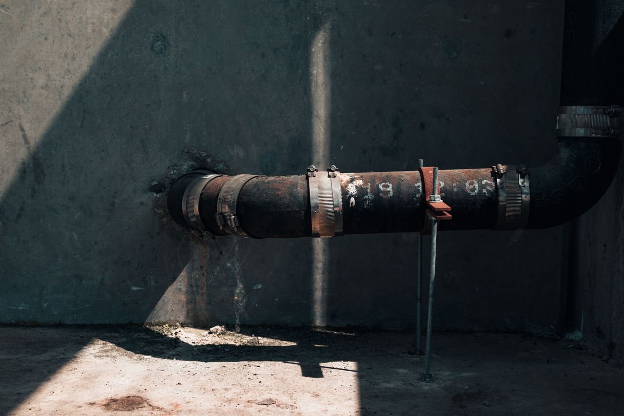 creative-02 Rusted industrial pipe on a concrete wall with dramatic sunlight and shadows, showcasing urban decay.